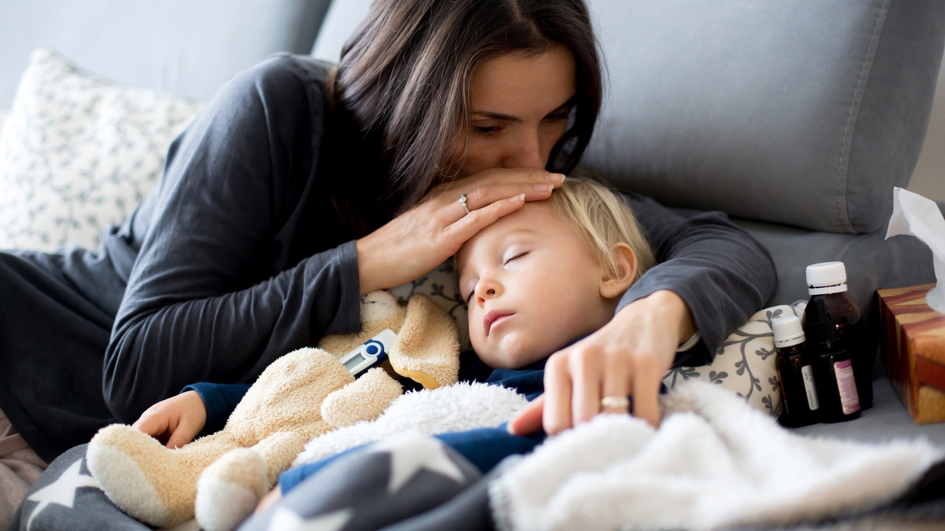 Mama caluje po glowie chore dziecko lezace w lozku