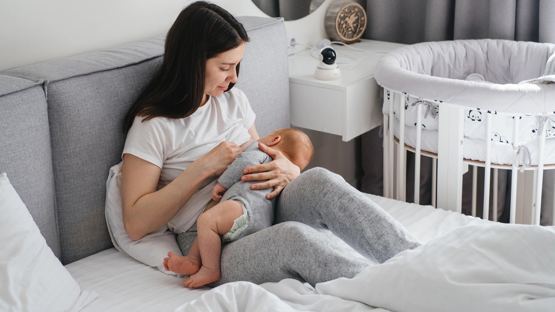Mloda mama karmi piersia niemowle siedzac na lozku