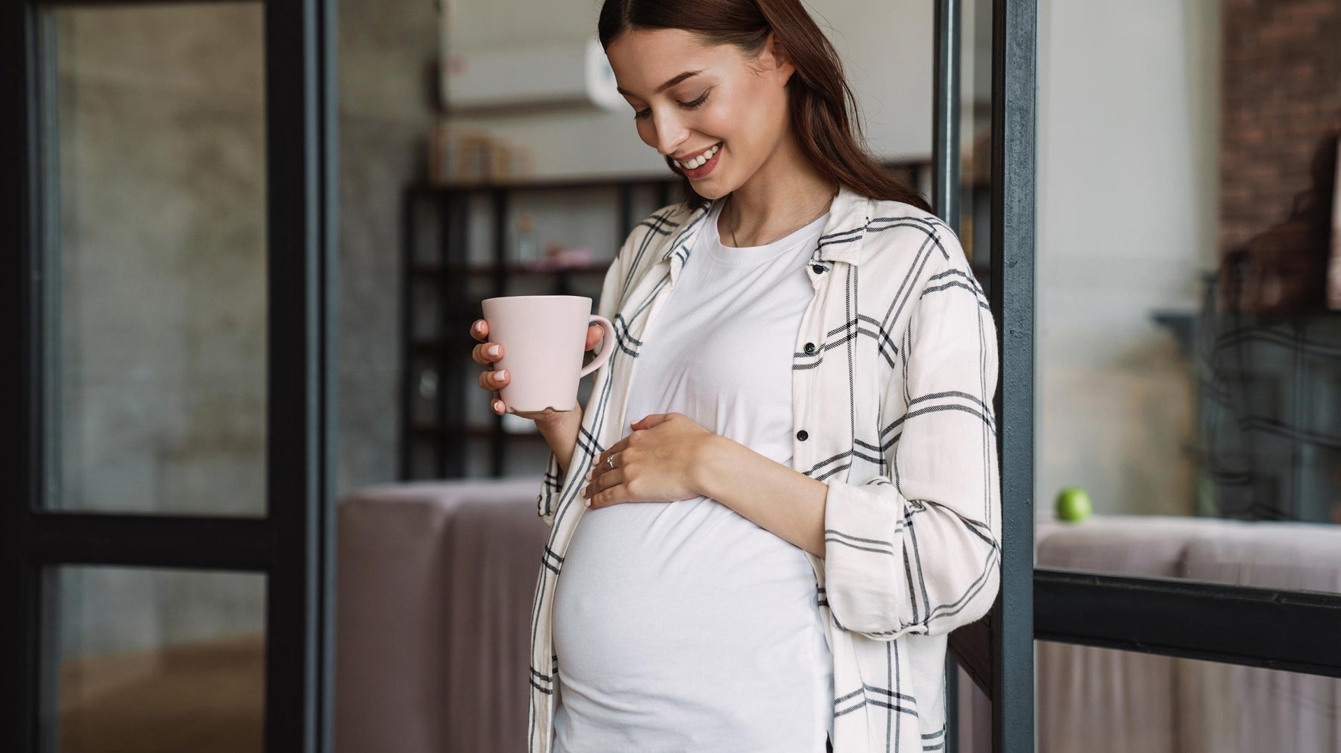 Mama trzyma w reku kubek i patrzy sie na ciezarny brzuch