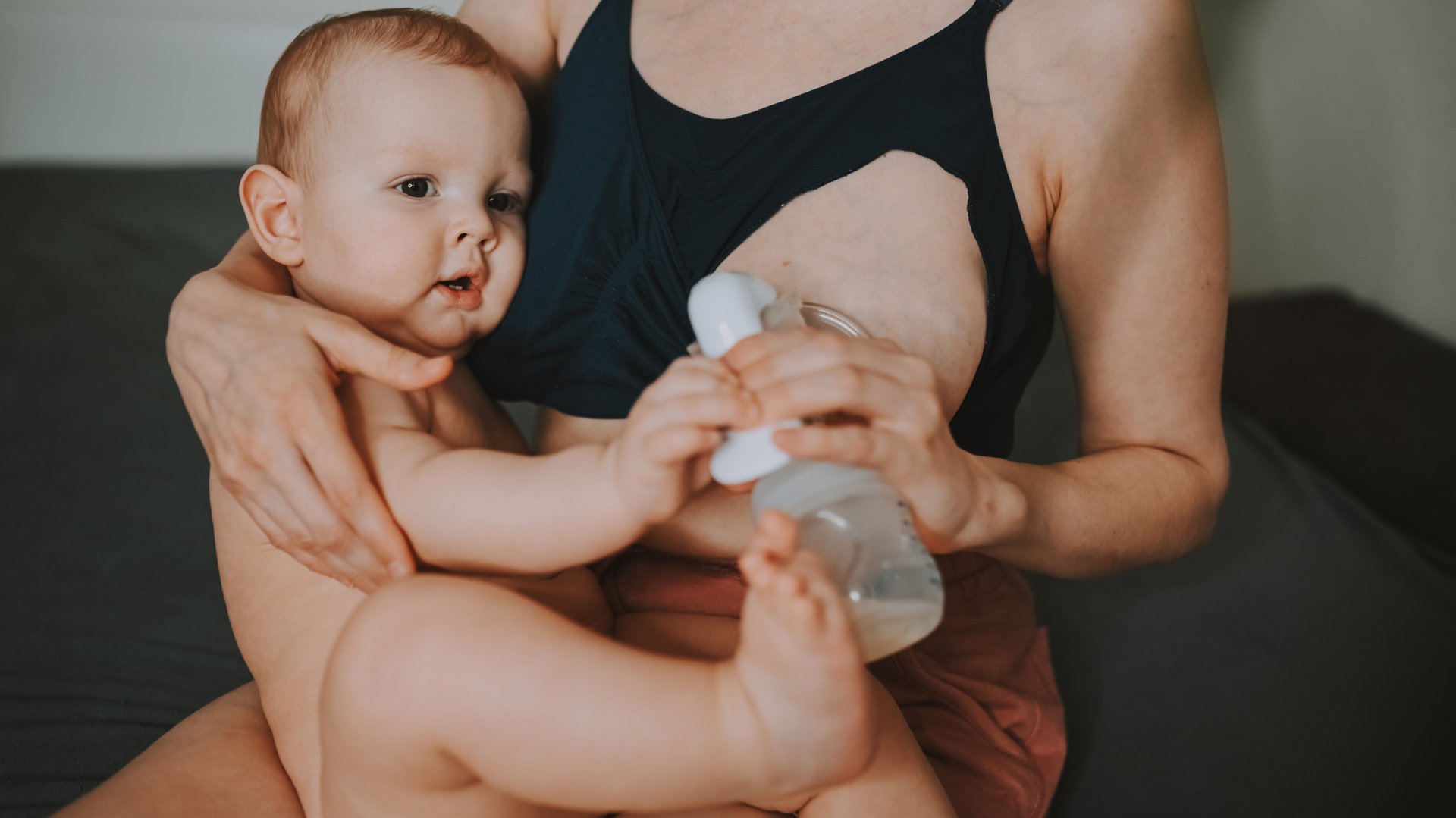 Mama trzyma dziecko na kolanach przykladajac laktator do piersi