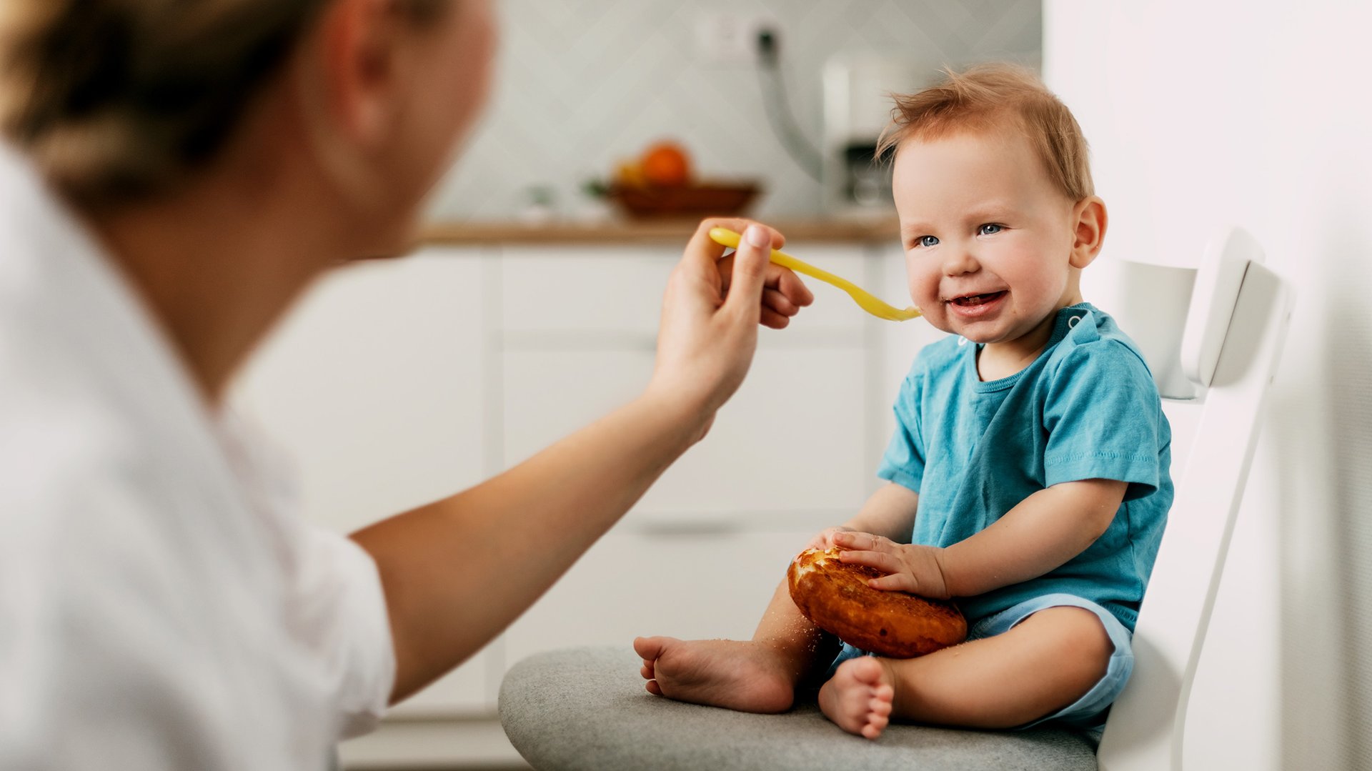 Mama karmi dziecko trzymajace w reku chleb lyzeczka