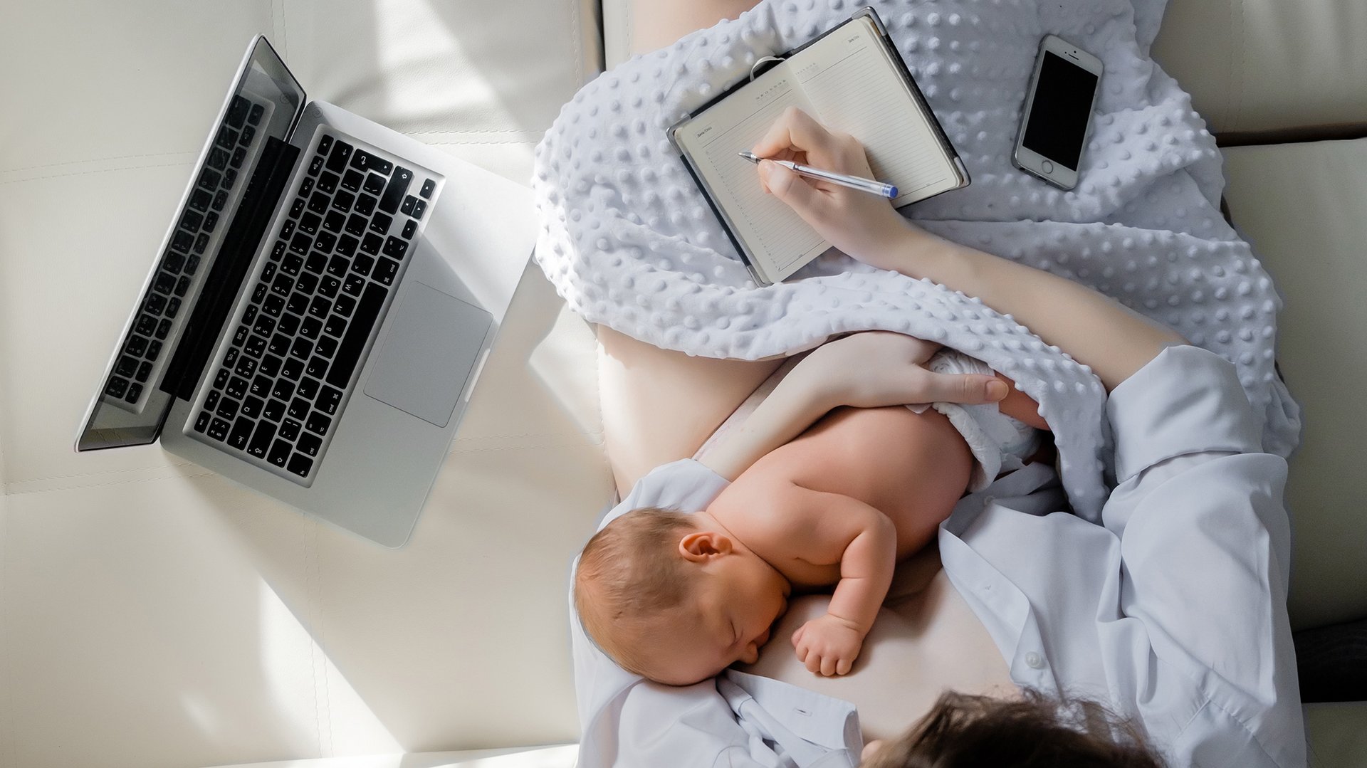 Pracujaca mama karmi dziecko piersia siedzac na lozku