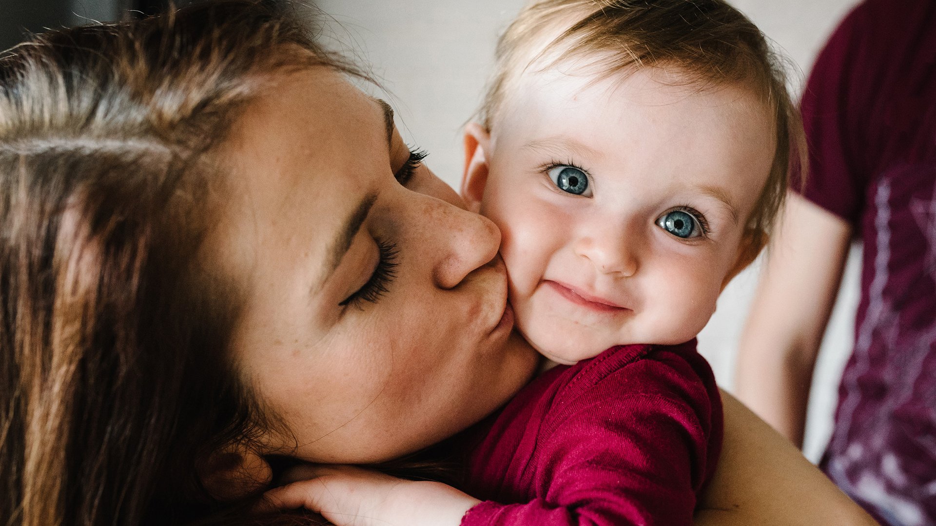 Mama caluje dziecko z szeroko otwartymi oczami w policzek