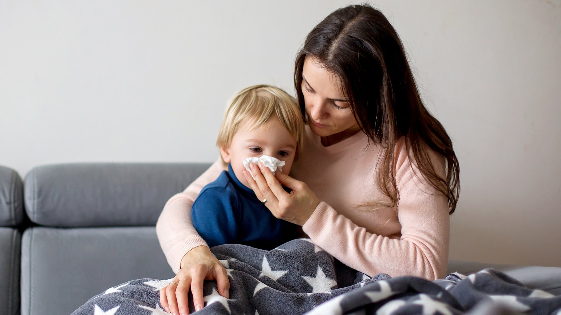 Mama wyciera nos przeziebionemy dziecku siedzac pod kocem